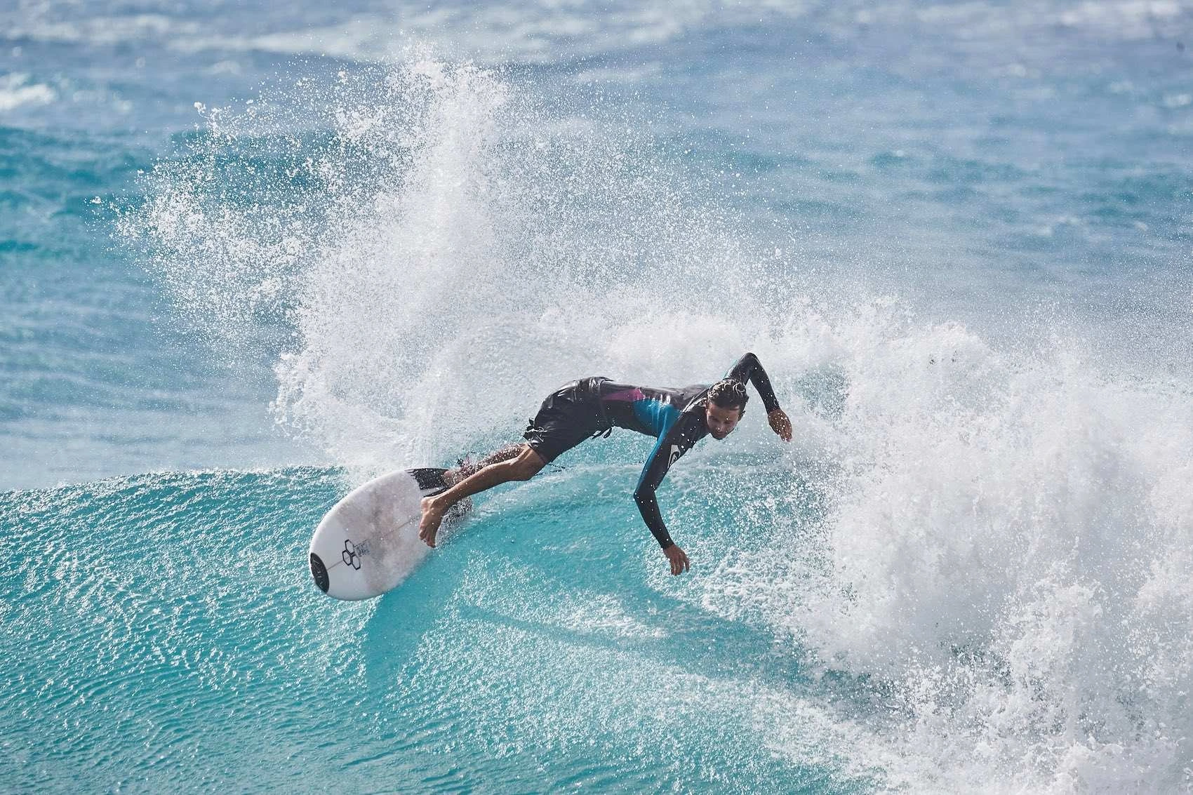 Surfer stretching forward through a cloud of spray — photograph by Michaël Gramm